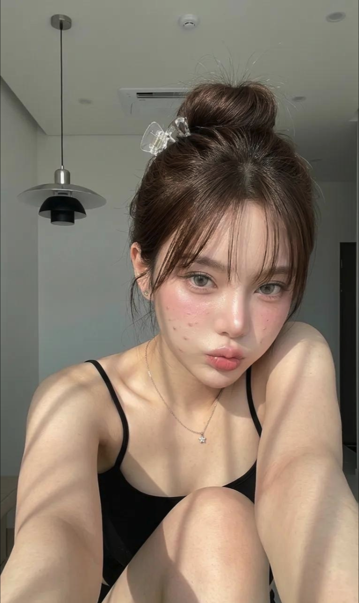 A woman posing for a close-up selfie indoors, wearing a black camisole and a hair clip.