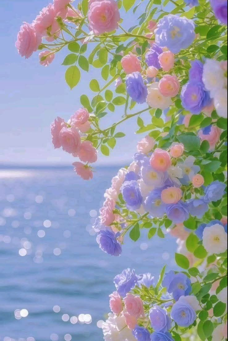 Clusters of pastel pink, blue, and white roses with green foliage against a sparkling blue sea.