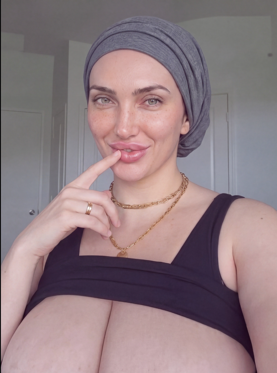 A woman in a gray head wrap touching her lip with her index finger indoors.