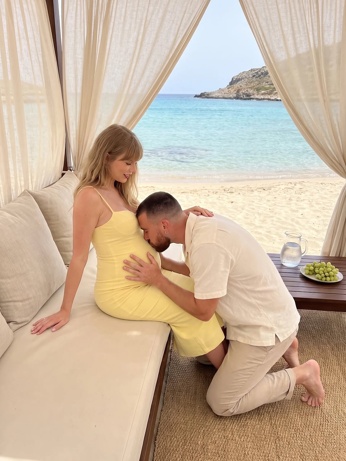 A woman resembling Taylor Swift seated on a daybed and a man resembling Travis Kelce kneeling to embrace her belly at a beach cabana.