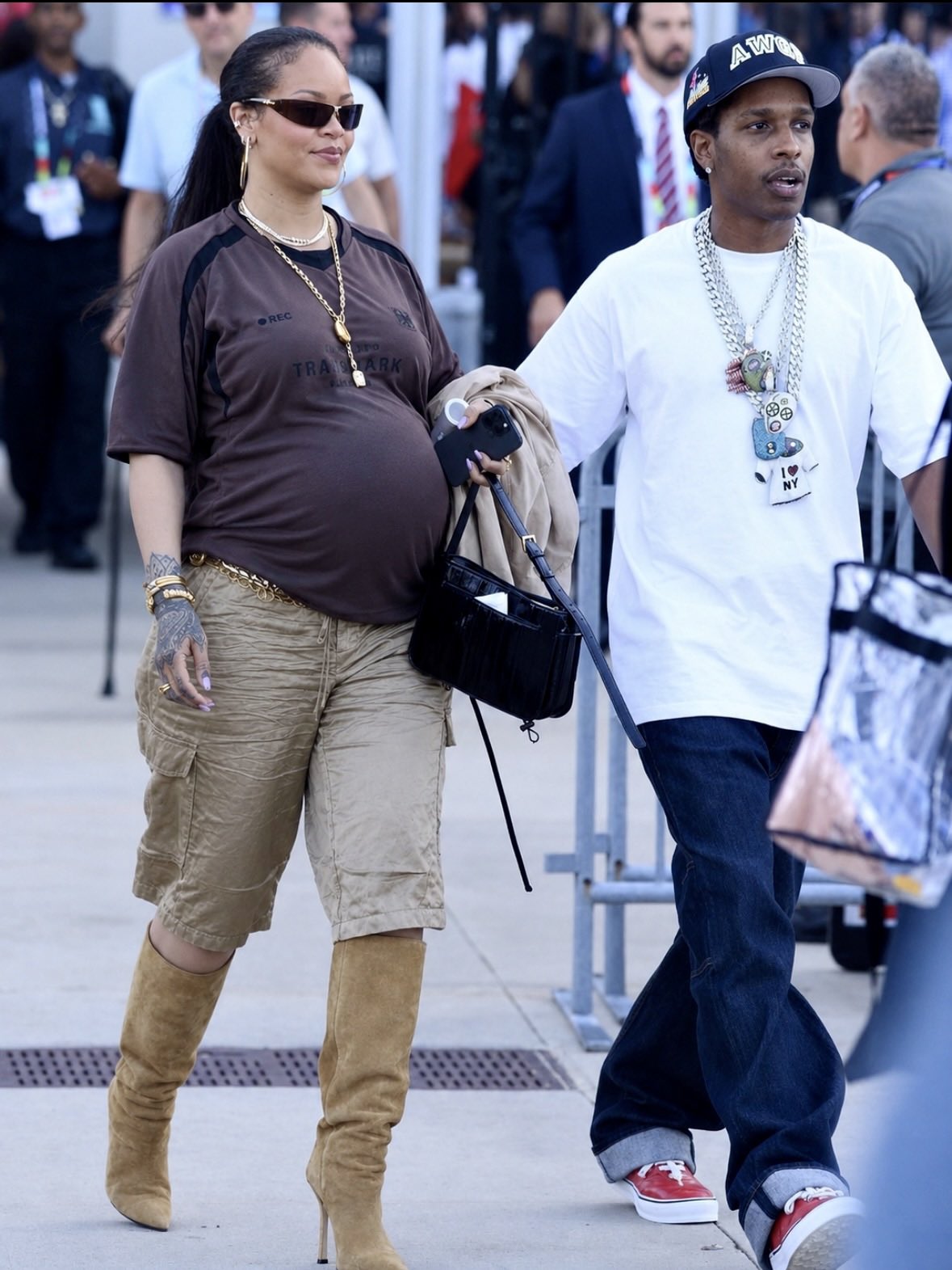 A woman resembling Rihanna and a man resembling A$AP Rocky walking together outdoors, with the woman visibly pregnant.
