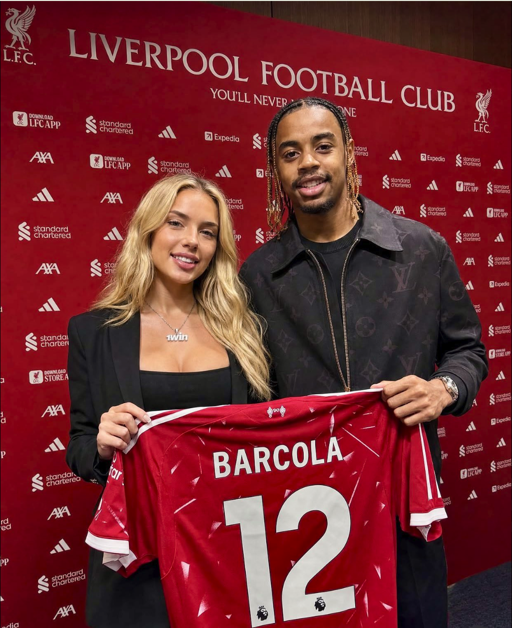 A man resembling Robert Ri'chard and a woman holding up a red Liverpool FC jersey reading 'BARCOLA 12'.
