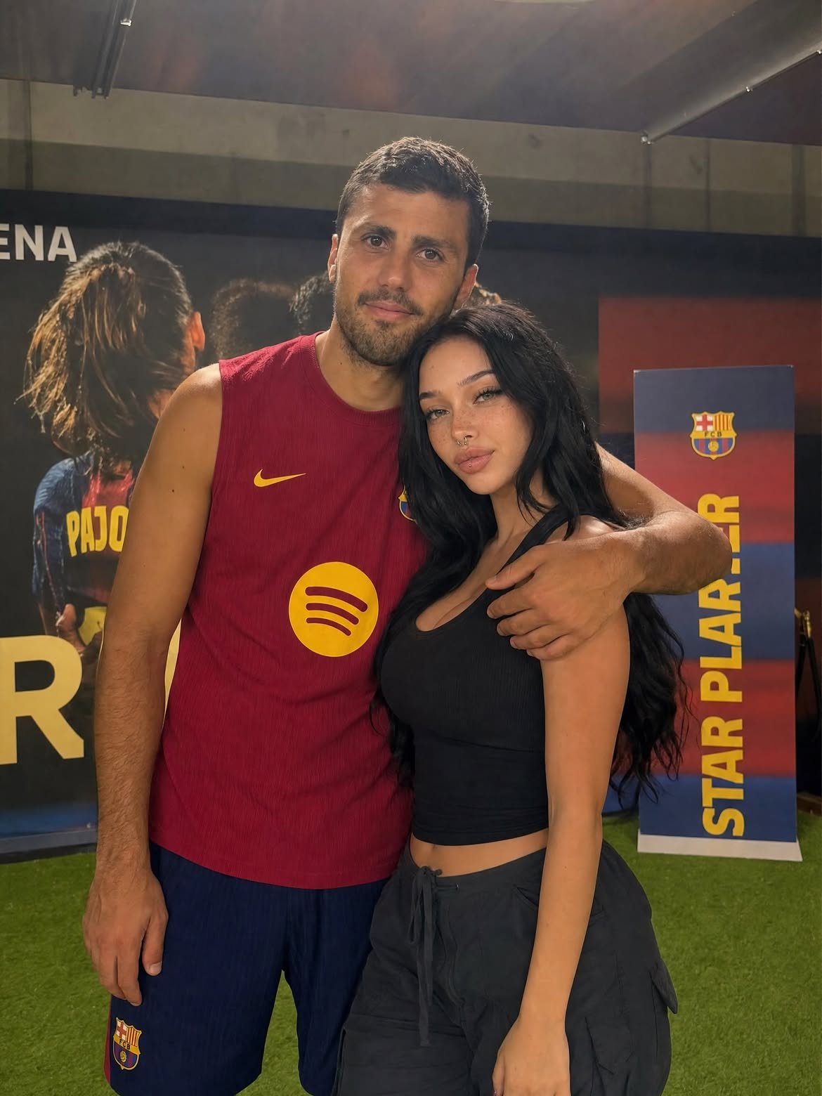 A man resembling Rodri in an FC Barcelona kit posing with a woman in a black tank top at a promotional event.