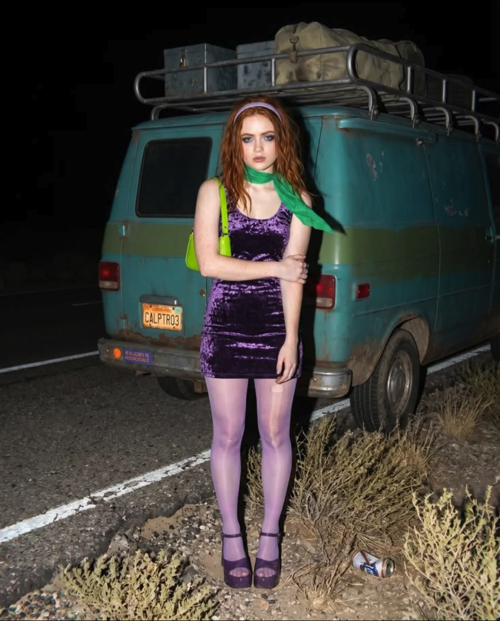 A young woman resembling Sadie Sink standing in front of a teal vintage van at night, wearing a purple velvet dress with a green neck scarf.