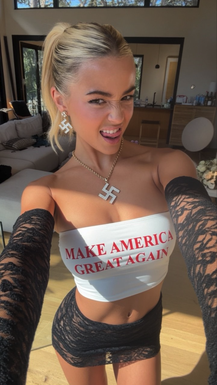 A woman taking a selfie in a 'Make America Great Again' tube top with swastika-style jewelry.