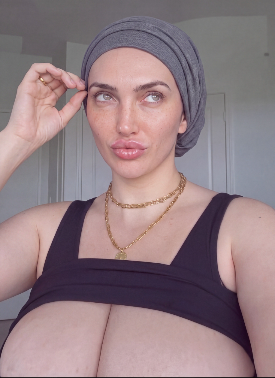 A woman wearing a gray head wrap and a black sleeveless top, posing for a selfie indoors.