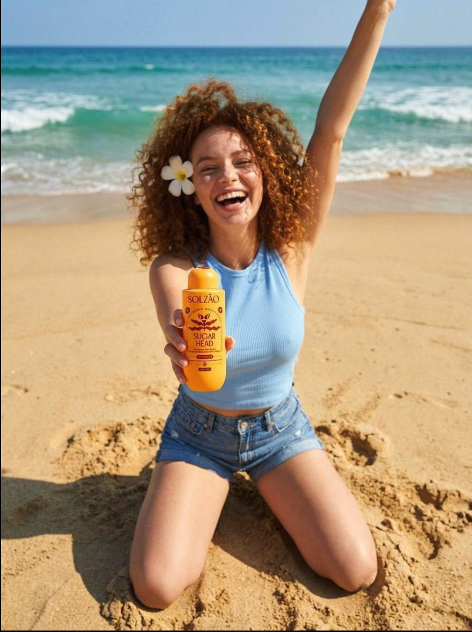 A woman with curly auburn hair kneeling on a beach holding a Solzão Sugar Head sunscreen bottle.