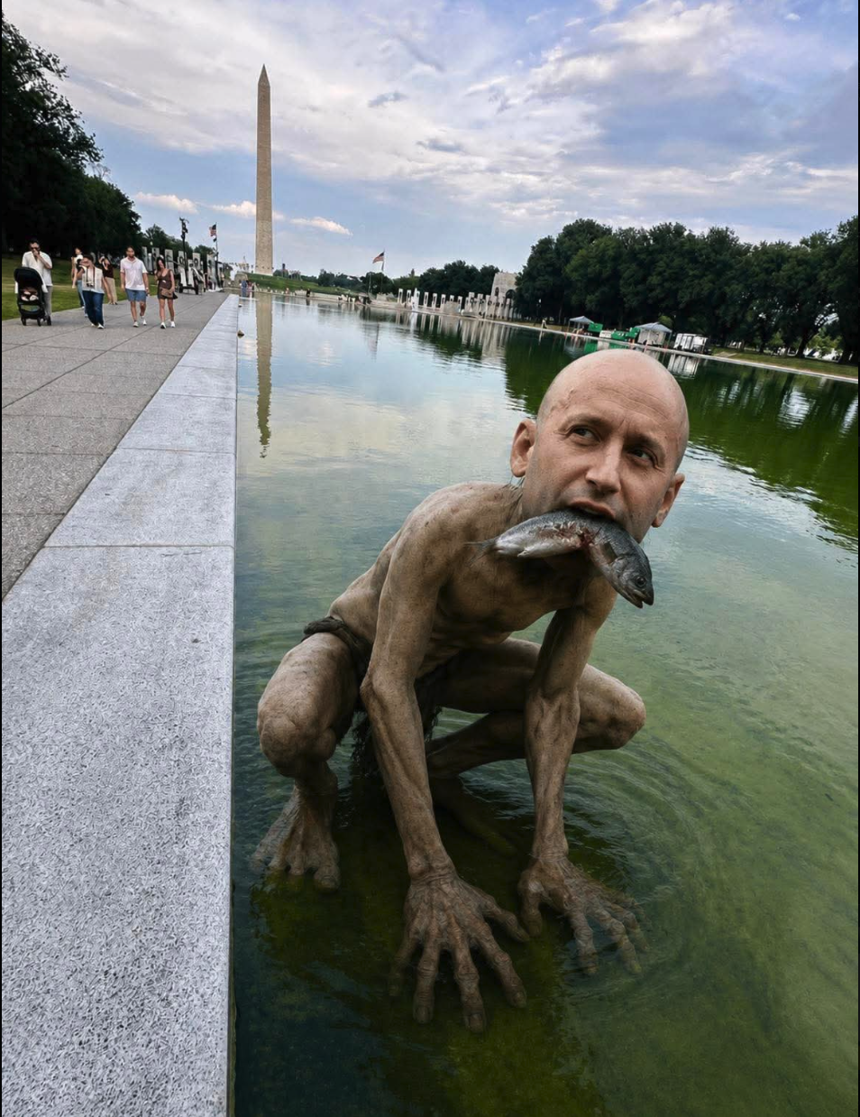 A mud-covered creature resembling Stephen Miller crouching in the WWII Memorial reflecting pool with a fish in its mouth.