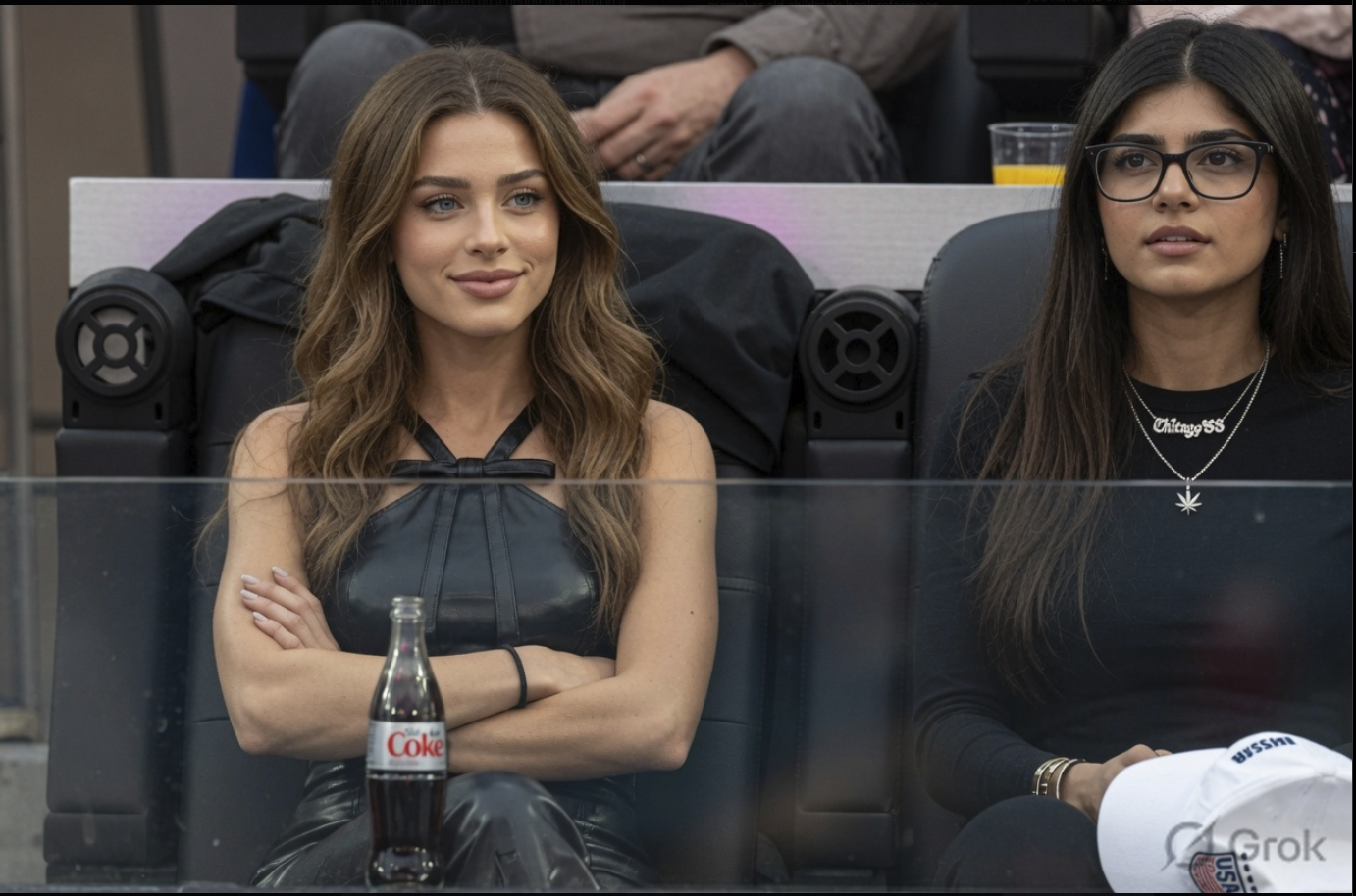 A woman resembling Taylor Hill seated in arena suite seating beside another woman, with a Diet Coke bottle in front of her.
