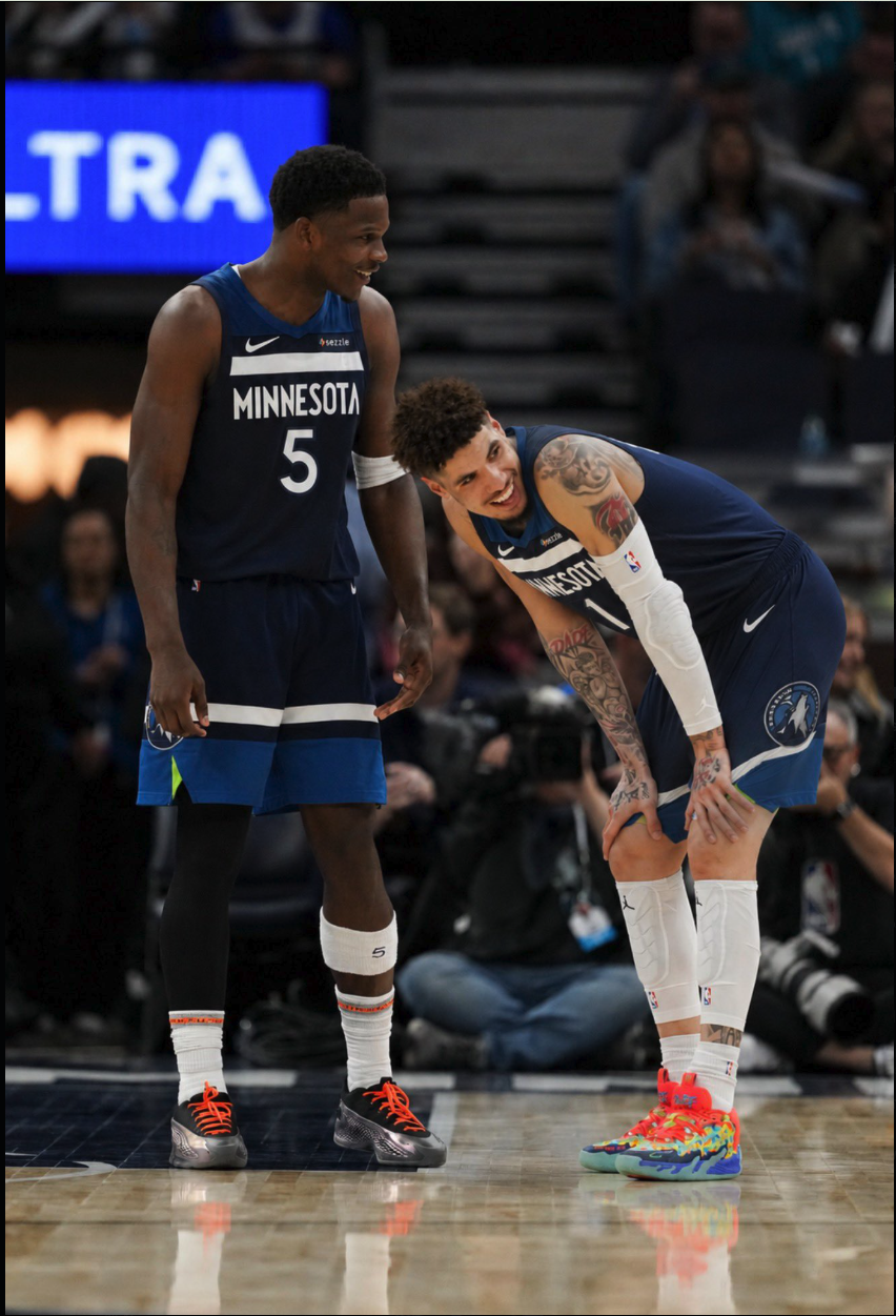 Two basketball players in Minnesota Timberwolves uniforms laughing together on a court.