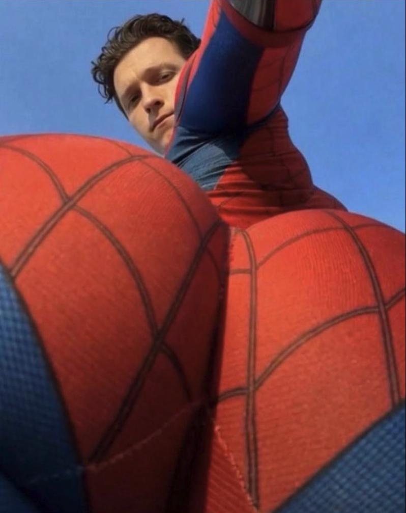 A man resembling Tom Holland wearing a red and blue Spider-Man costume against a blue sky.