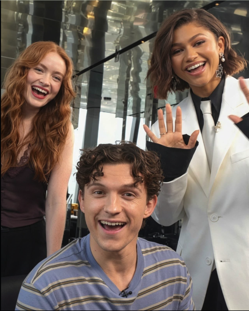 Three people resembling Tom Holland, Zendaya, and Sadie Sinks laughing together indoors.