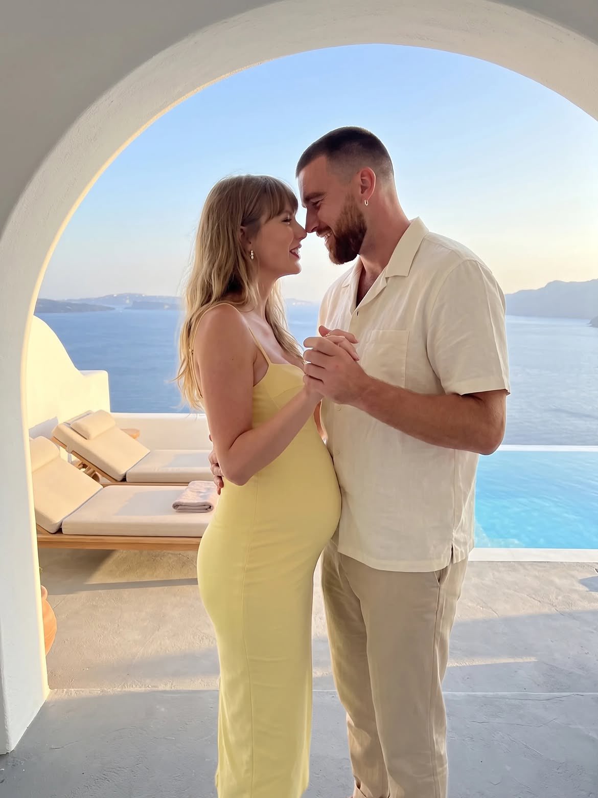 A man and a woman resembling Travis Kelce and Taylor Swift standing close together under a white arch overlooking the sea.