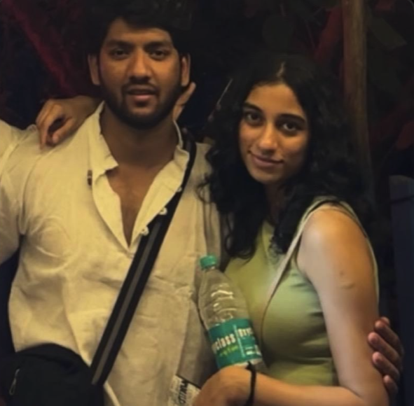 A man in a white shirt and a woman in a green tank top posing together at a dimly lit indoor gathering.