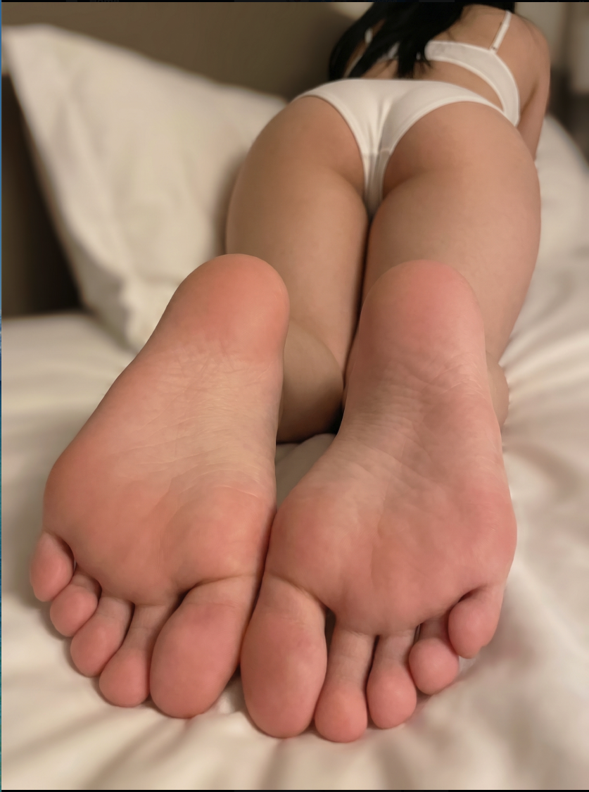 A person in white underwear lying face-down on a bed, with the soles of both feet extended toward the viewer.