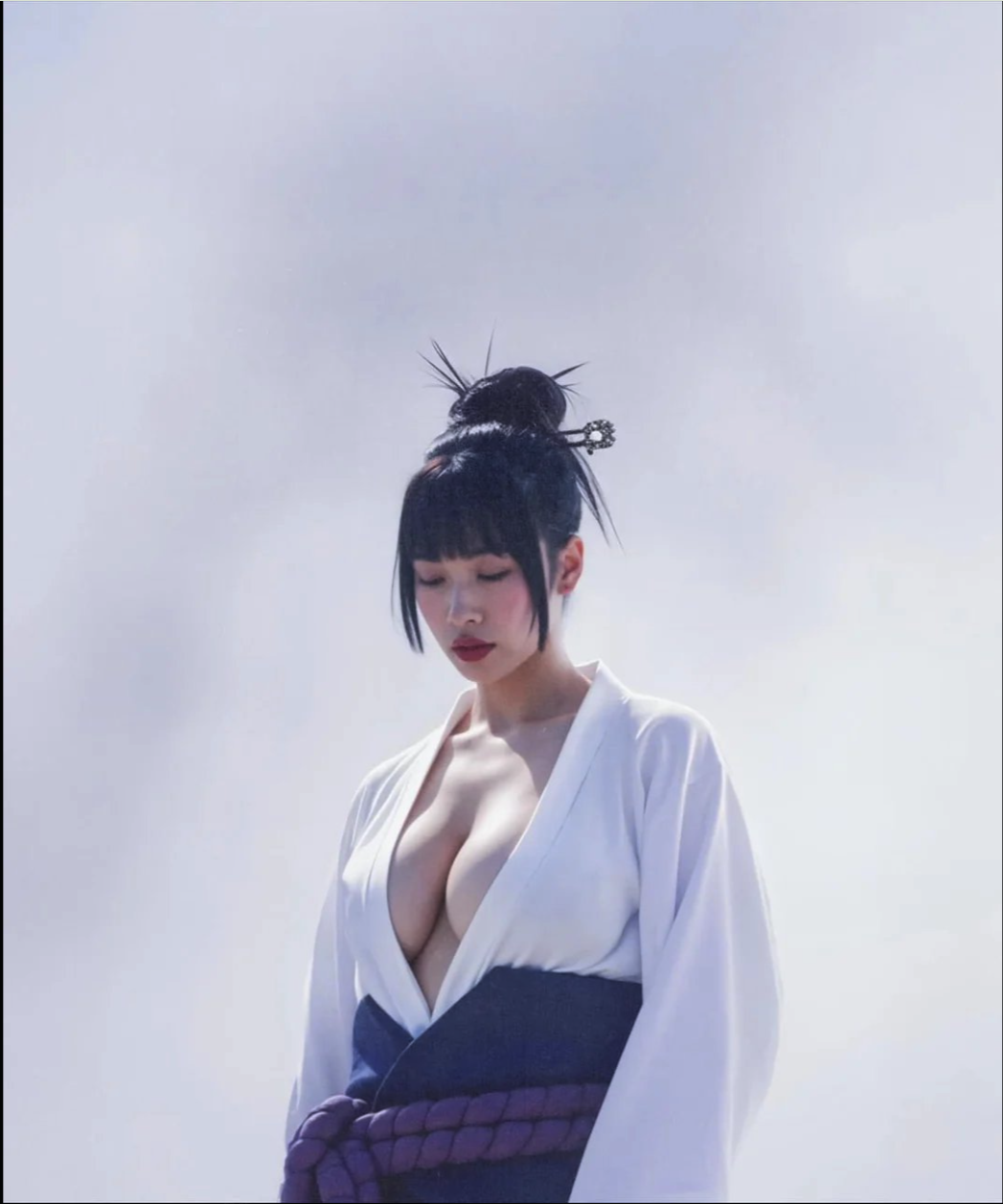 A woman with dark hair in an updo wearing a white kimono-style top with a deep neckline and a dark sash.