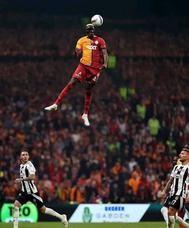 A man resembling Victor Osimhen in a Galatasaray jersey jumping to head a ball, with two players in Beşiktaş kits on the field.