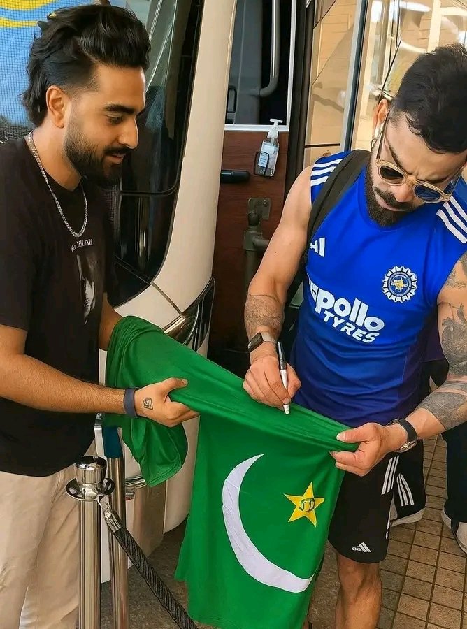 Two men, one resembling Virat Kohli in a blue India cricket jersey, signing a green Pakistan-style jersey beside a vehicle.