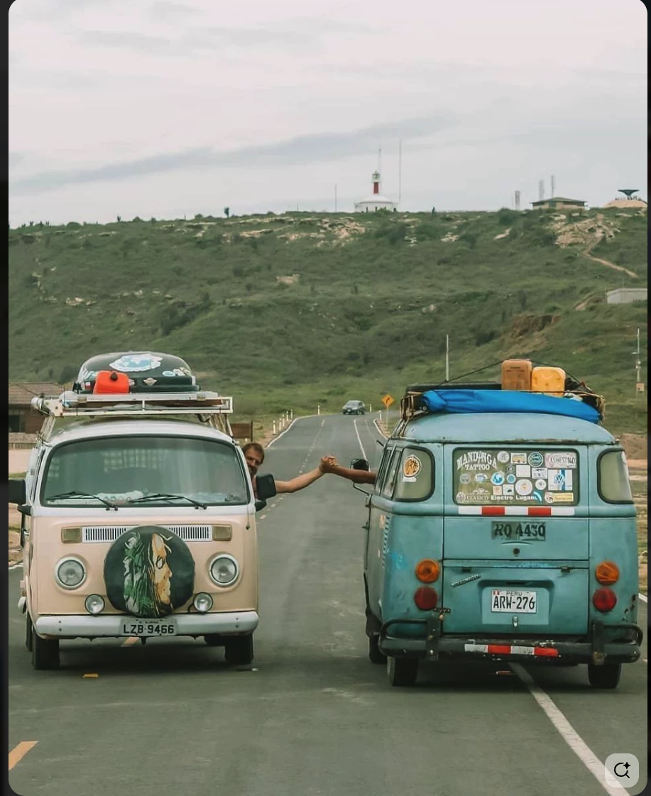 Two Volkswagen camper vans driving on a road, with their drivers fist-bumping through their open side windows.