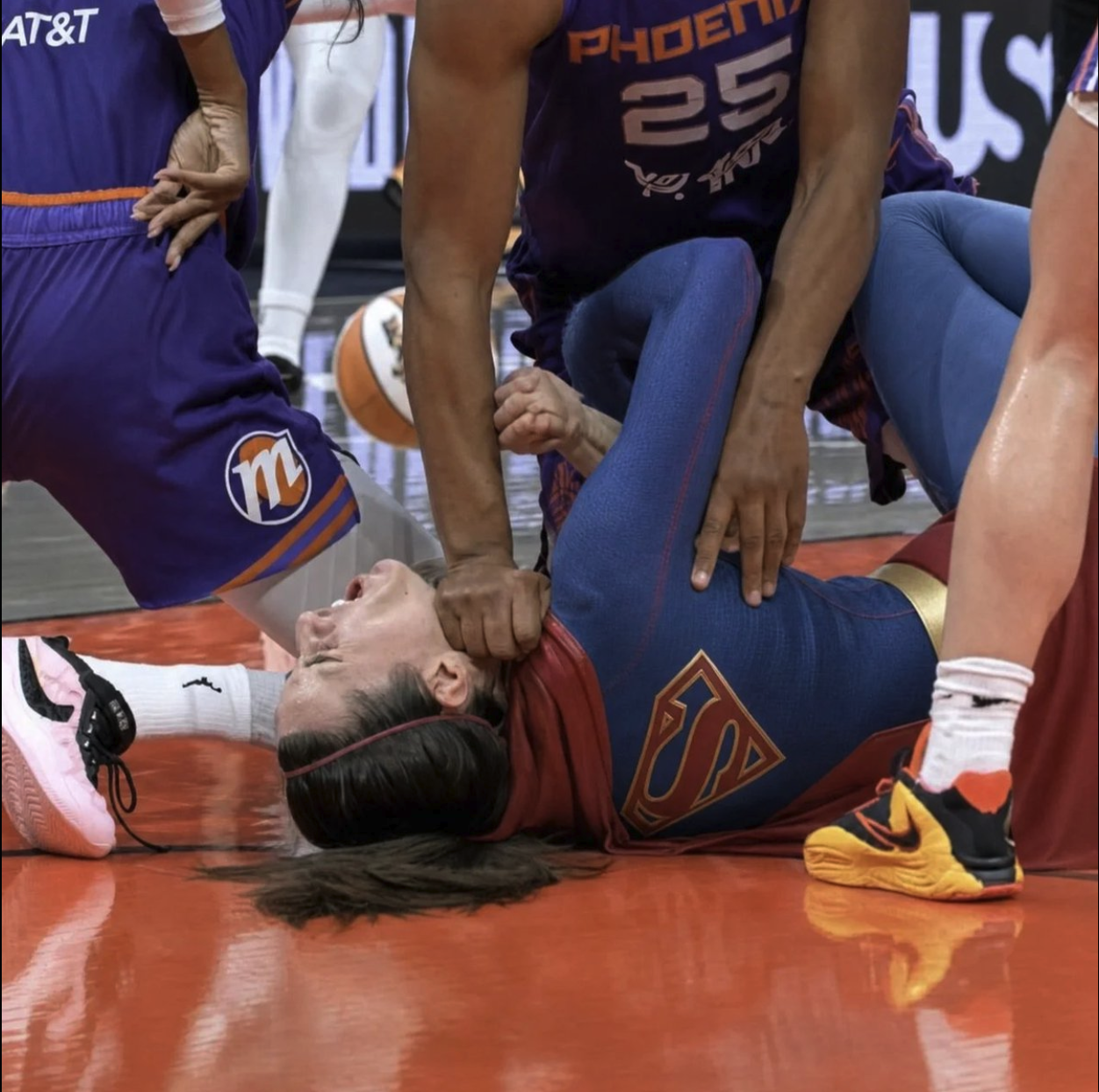 A women's basketball player lying face-up on the court while a Phoenix Mercury player stands over her.
