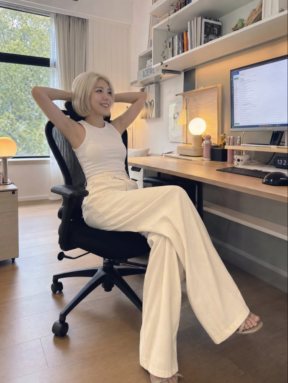 An unidentified woman with short blonde hair seated at a home office desk with her hands behind her head.