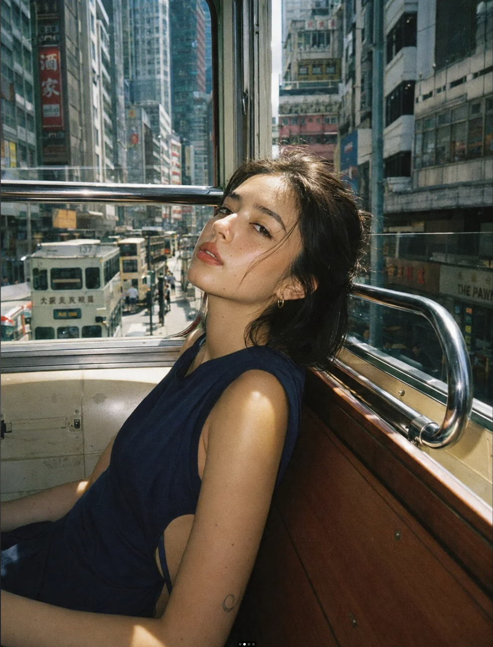 A young woman with dark hair seated inside a tram, with a busy Hong Kong street visible through the window behind her.