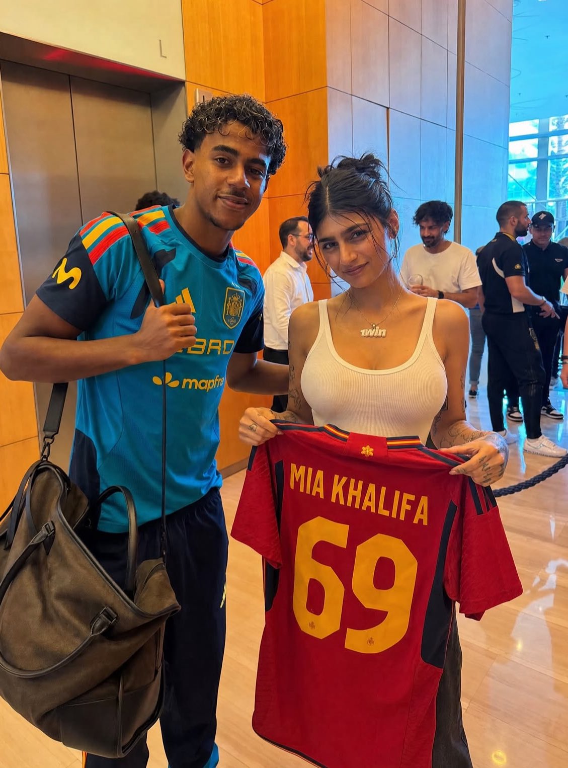A man resembling Lamine Yamal standing beside a woman resembling Mia Khalifa holding a red Spain national team jersey reading 'MIA KHALIFA 69'.