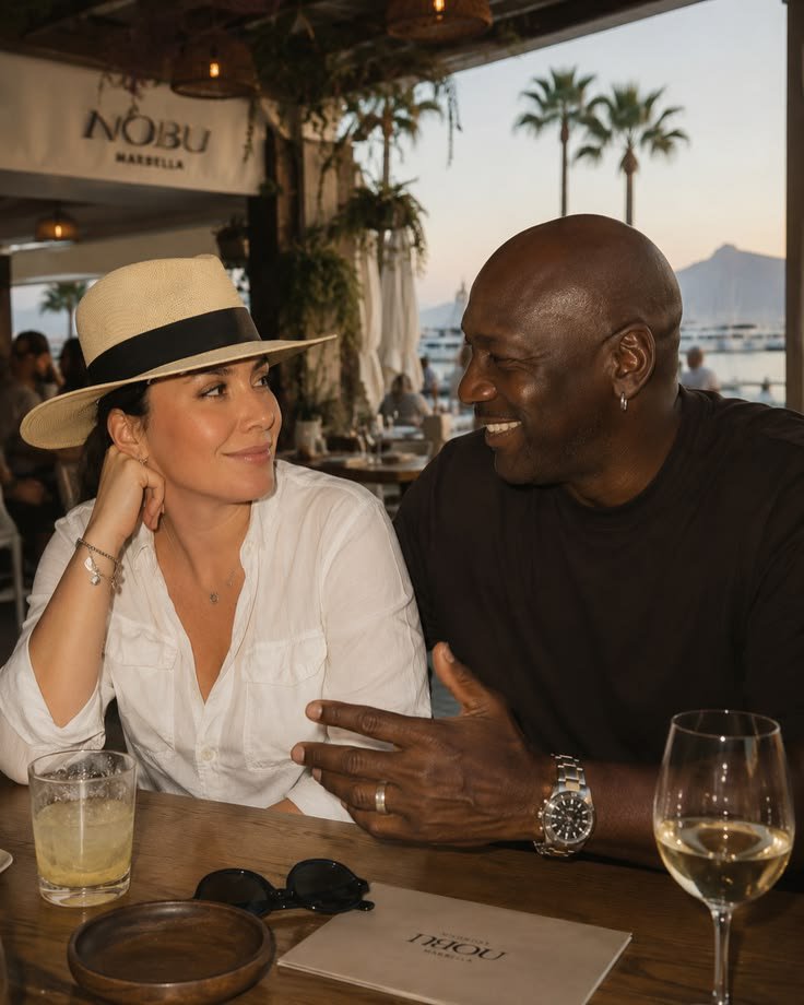 AI Michael Jordan and a woman seated at a wooden table inside Nobu Marbella restaurant, smiling at each other.