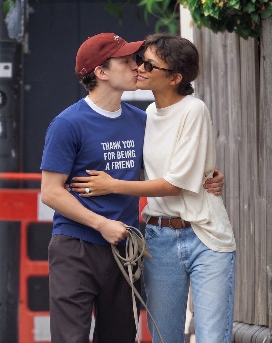 A woman resembling Zendaya and a man resembling Tom Holland kissing on a sidewalk.