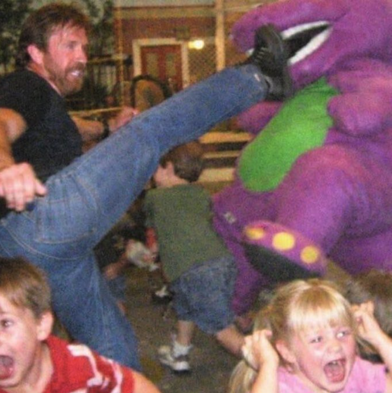 A man appearing to deliver a roundhouse kick to a Barney the Dinosaur mascot at an indoor event, with two children reacting in the foreground.