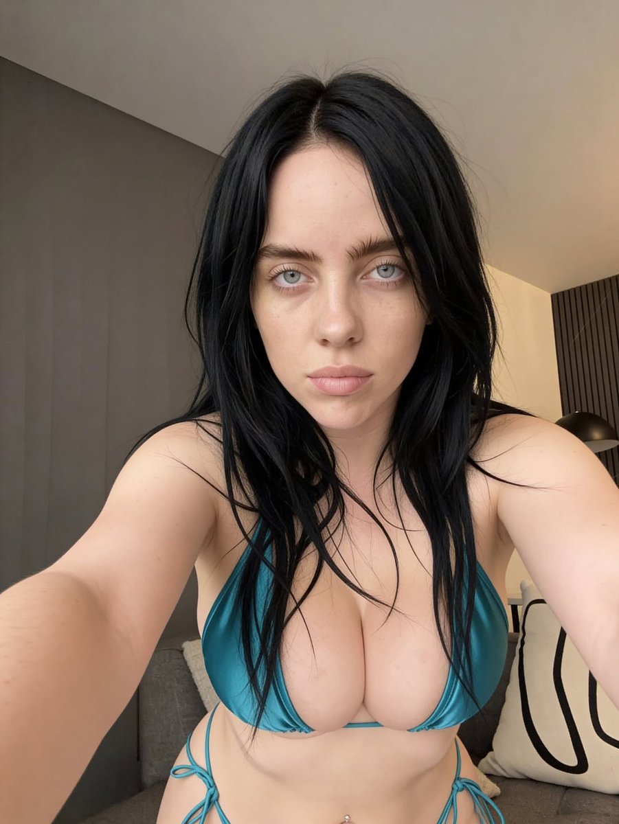 A woman resembling Billie Eilish in a teal bikini taking a selfie in a modern interior.