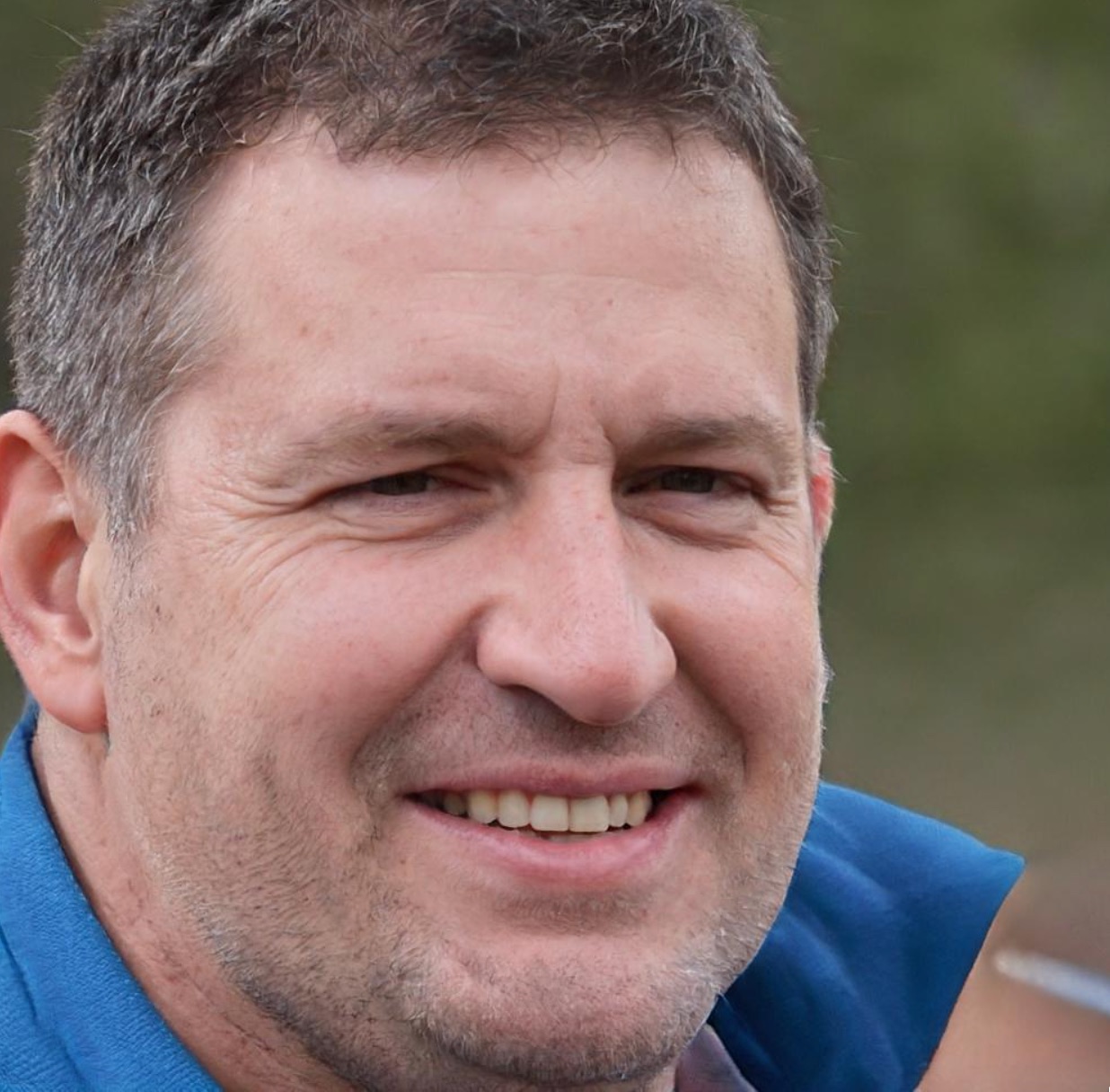 A close-up of a man resembling UnitedHealthcare CEO Brian Thompson smiling outdoors in a blue jacket.