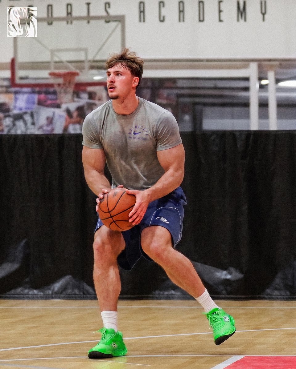 A basketball player resembling Cooper Flagg holding a ball on an indoor court at a Dallas facility.
