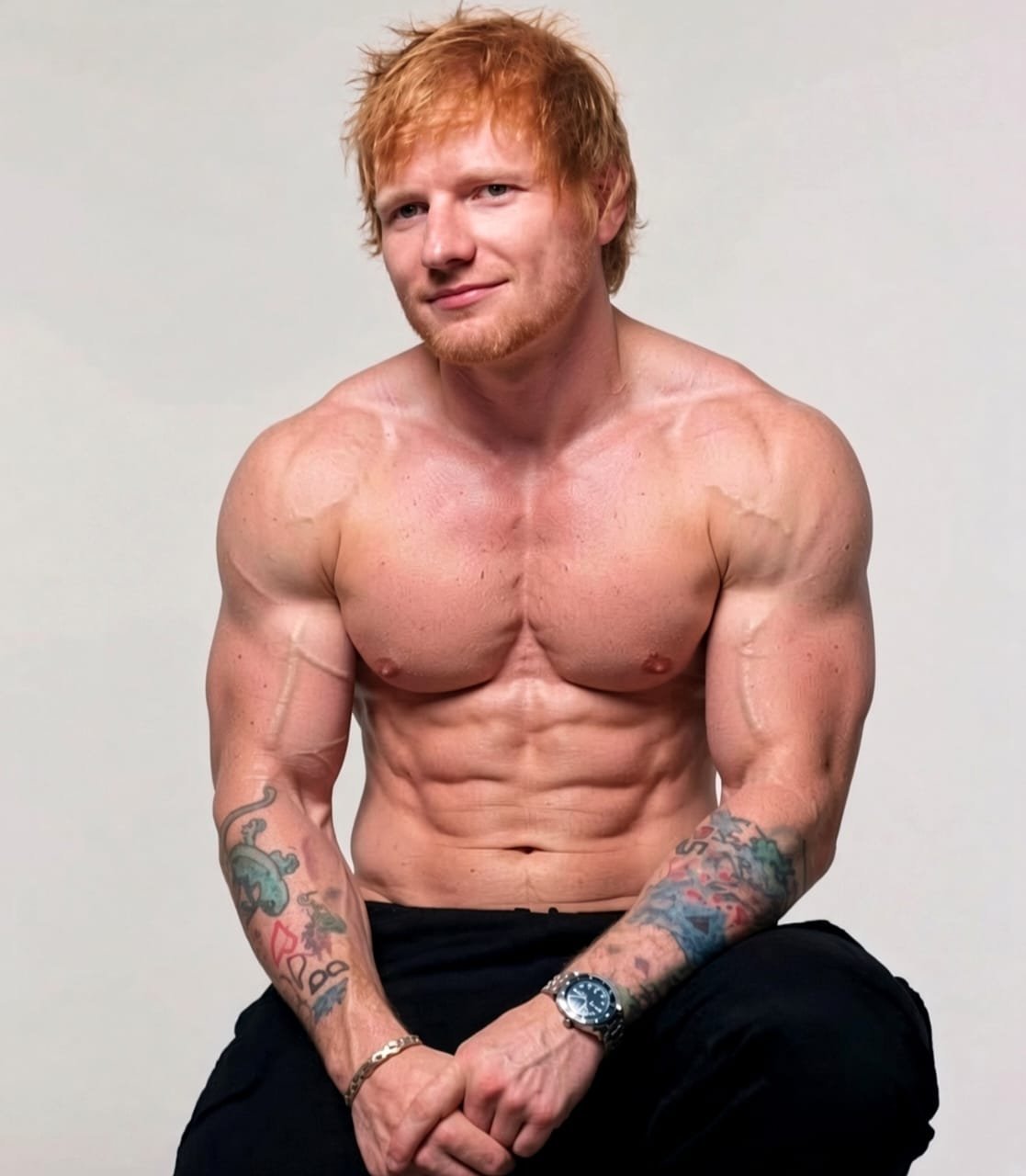 A man resembling Ed Sheeran seated shirtless against a plain background, showing a muscular build and tattooed forearms.