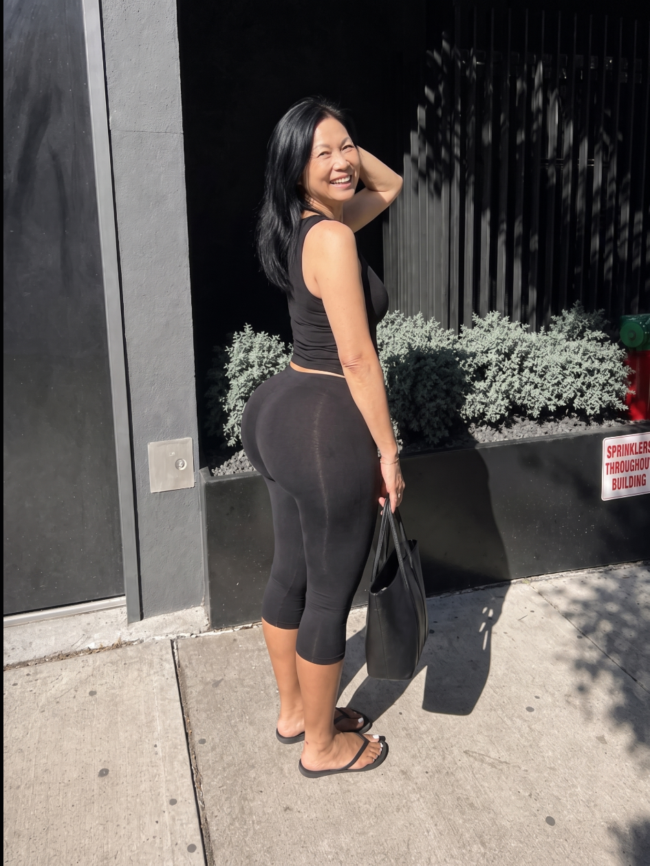 A woman smiling over her shoulder on a sidewalk.