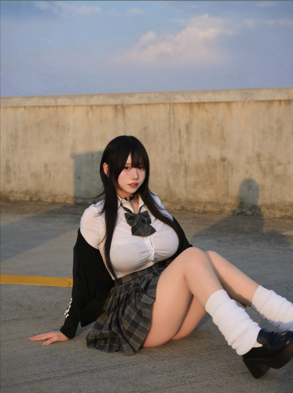 A woman resembling Enako in a school uniform cosplay seated on a concrete surface outdoors.