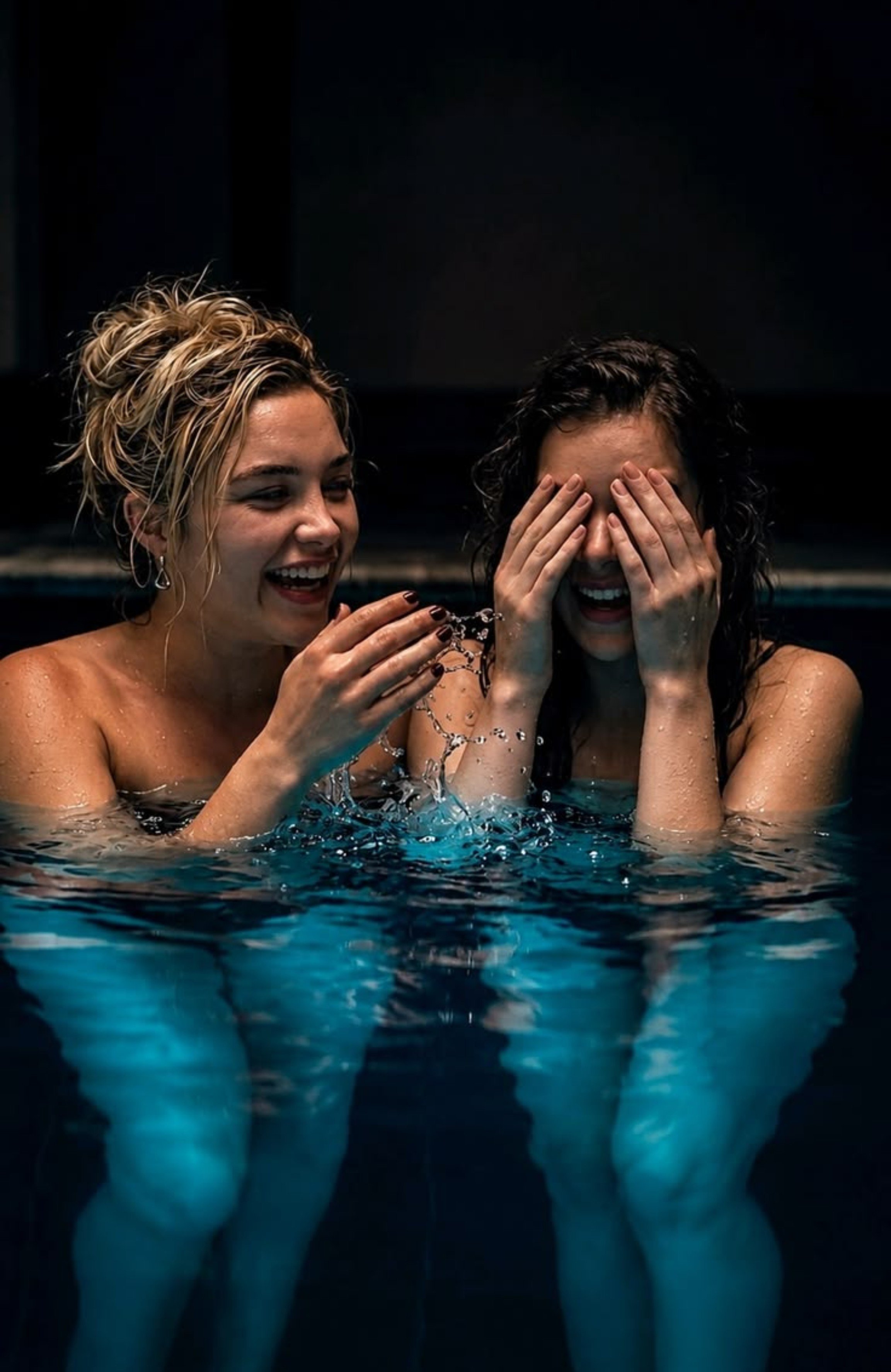 Two women resembling Florence Pugh and Hailee Steinfeld laughing together in a pool.