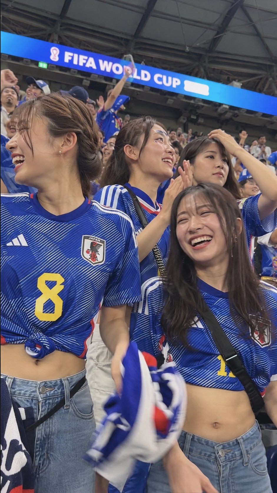 Women resembling Ikumi Hisamatsu and Alejandra Valencia celebrating in Japan national team jerseys at a FIFA World Cup match.