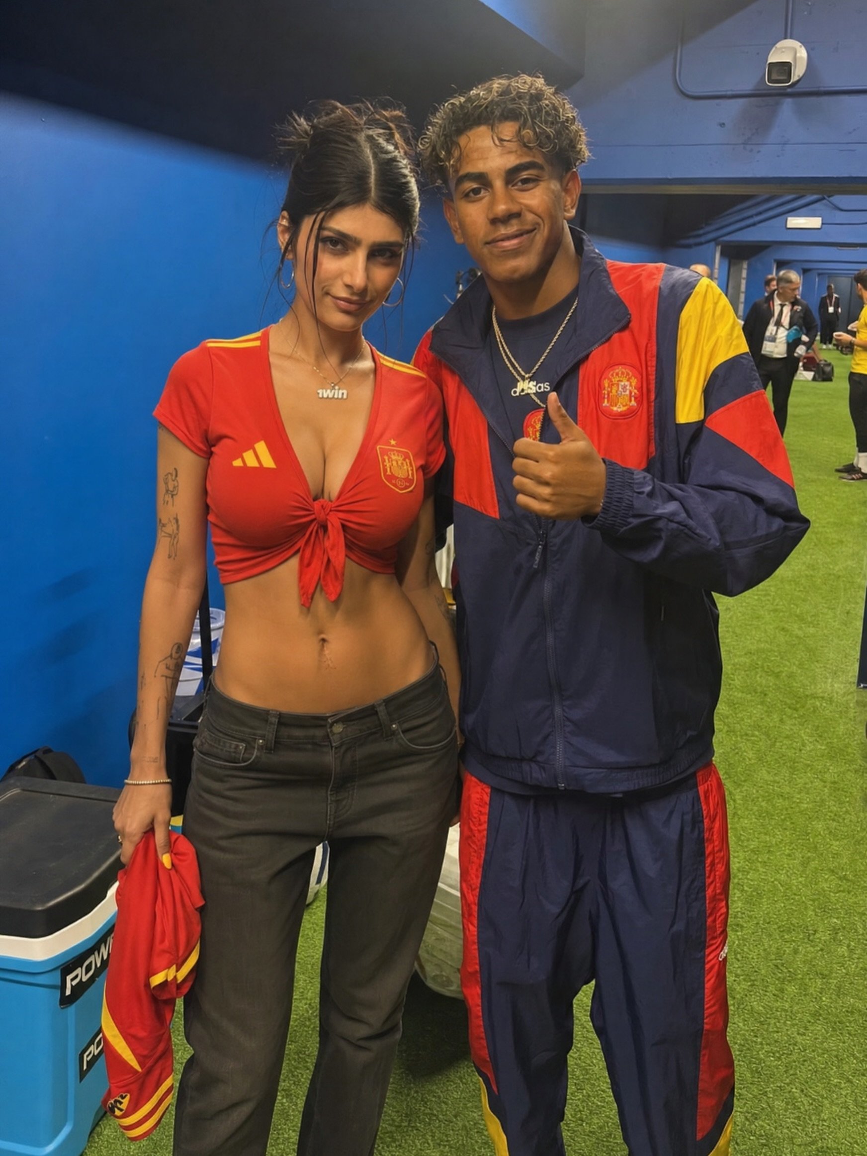 A woman resembling Mia Khalifa and a young man resembling Lamine Yamal posing together in Spain football attire in an indoor stadium area.