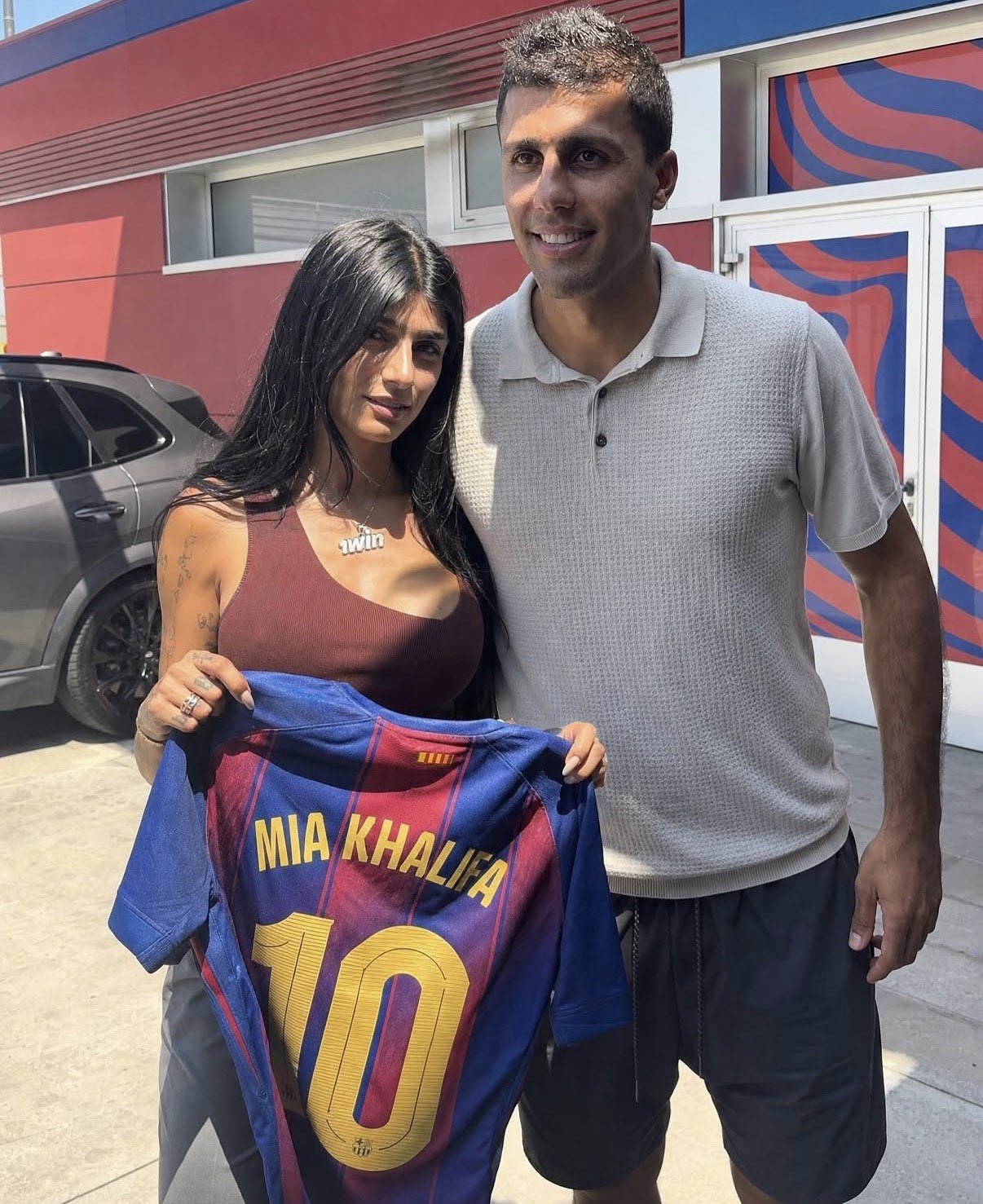 A woman and a man posing together outdoors, holding a Barcelona jersey reading 'MIA KHALIFA 10'.