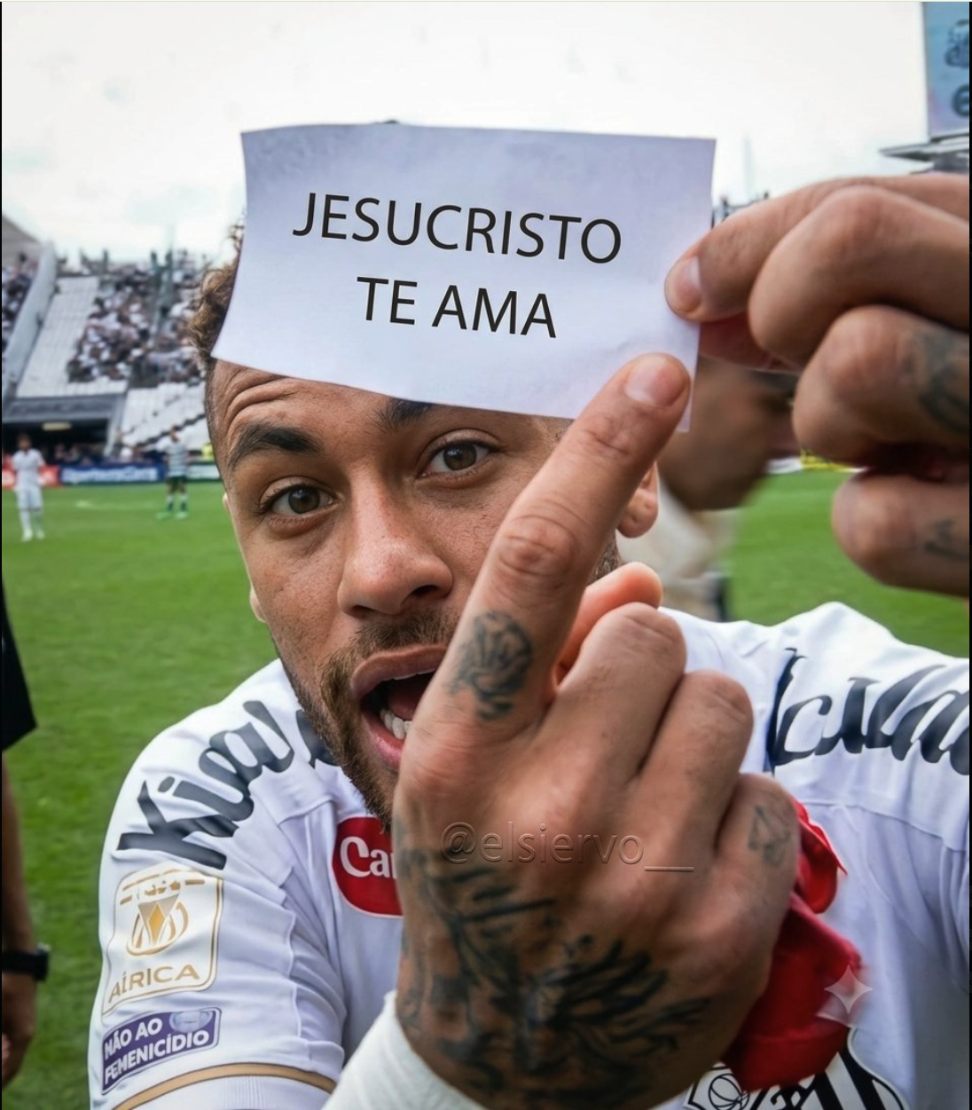 A man resembling Neymar holding a paper sign reading 'Jesucristo Te Ama' in front of his forehead on a soccer field.