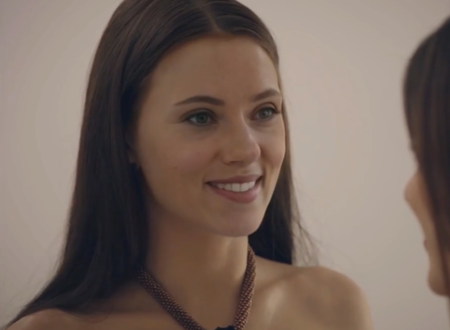 A woman resembling Scarlett Johansson smiling indoors against a neutral background.