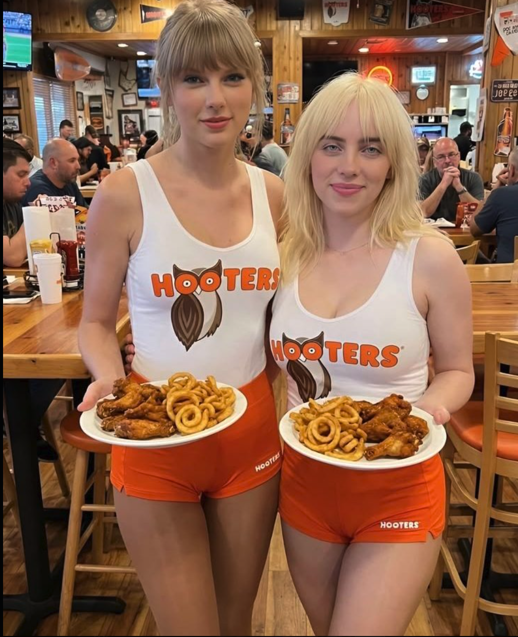 Two women resembling Taylor Swift and Billie Eilish wearing Hooters uniforms and holding plates of wings and onion rings.