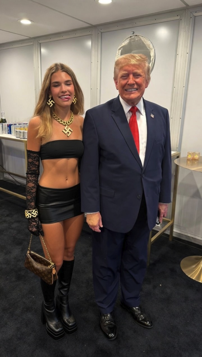 A man resembling Donald Trump in a dark suit standing beside a blonde woman in a black outfit indoors.