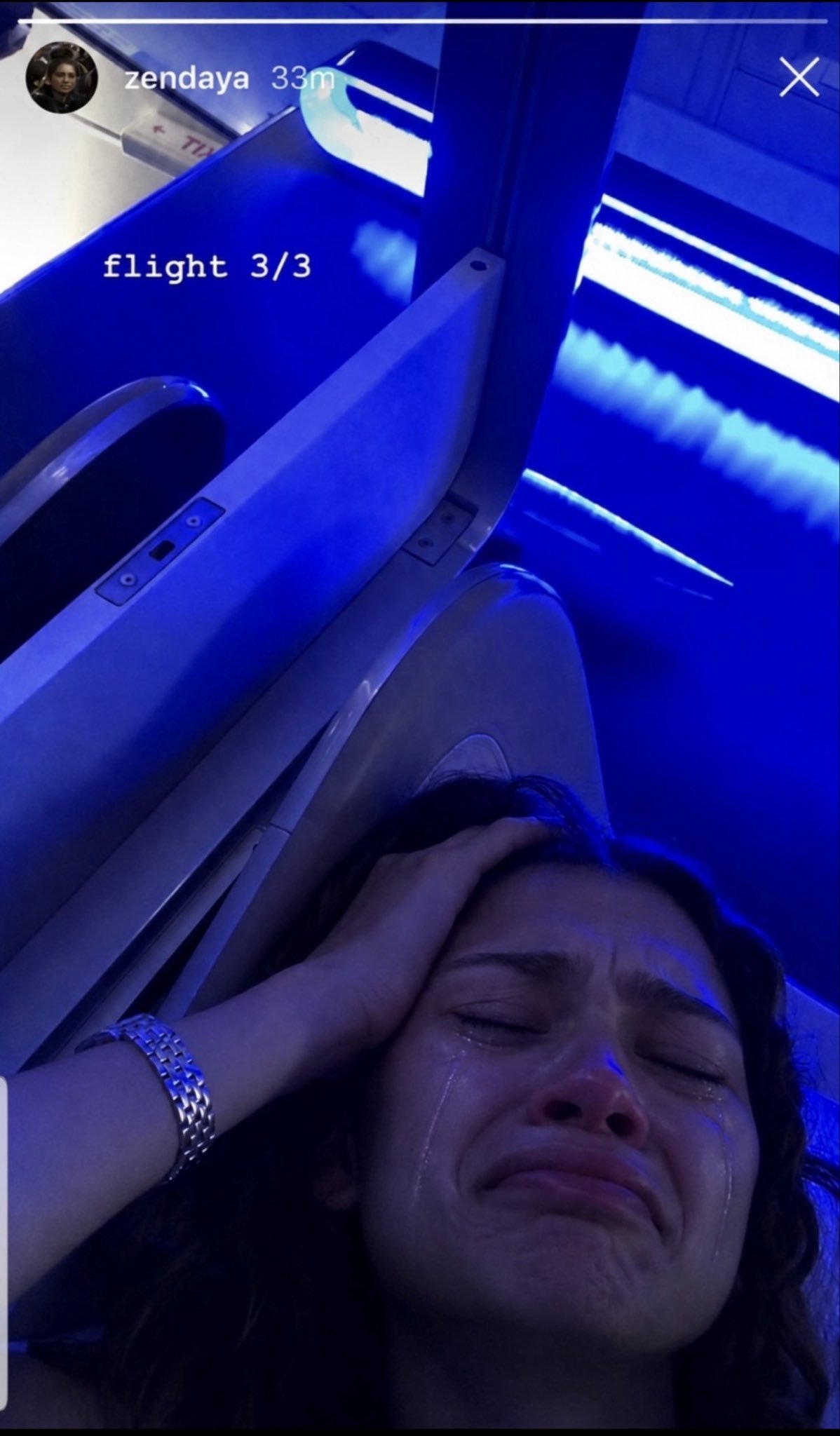A woman resembling Zendaya crying with her hand on her head inside a blue-lit airplane cabin, framed as an Instagram Story.