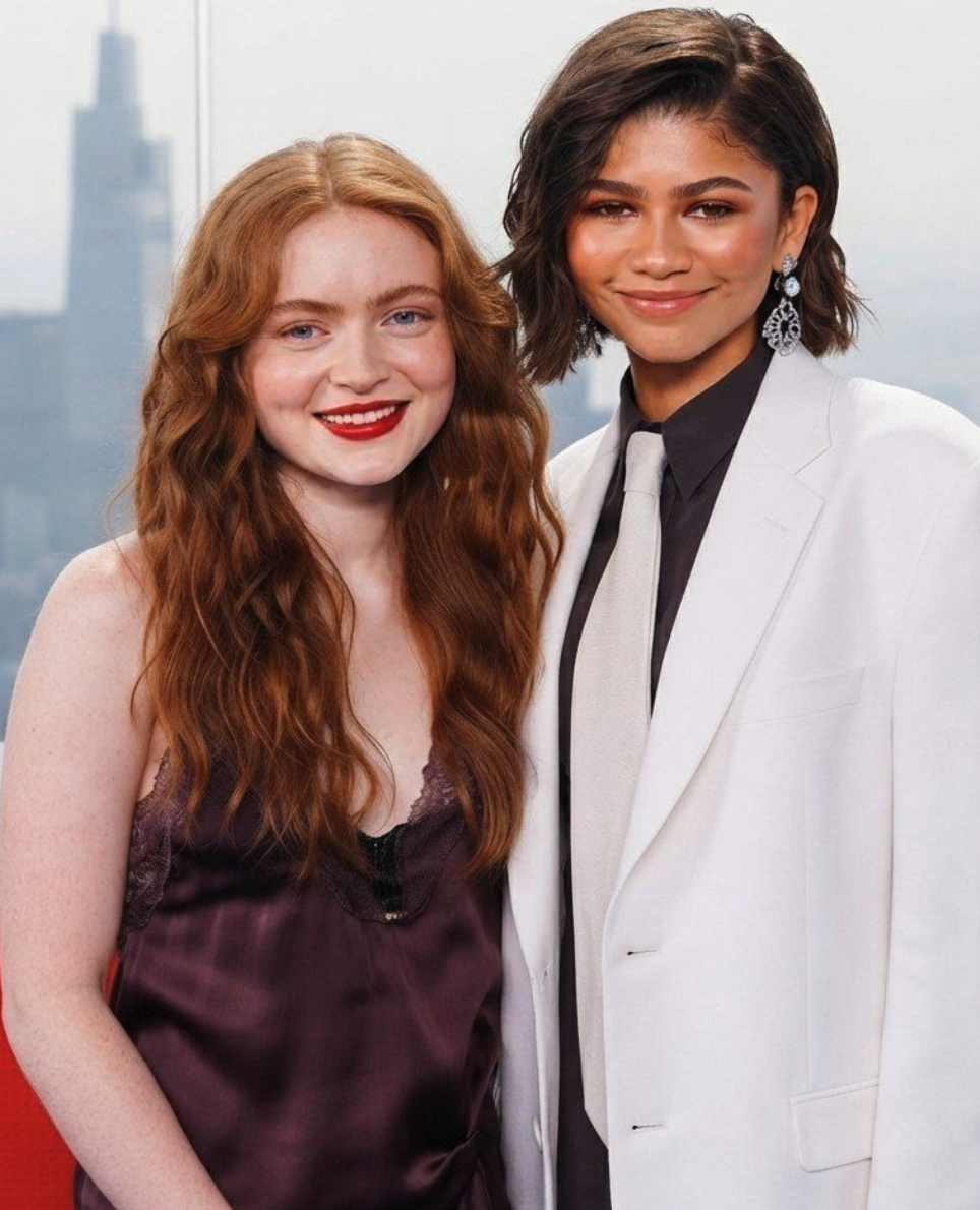 Two women resembling Zendaya and Sadie Elizabeth Sink posed together indoors at an event.