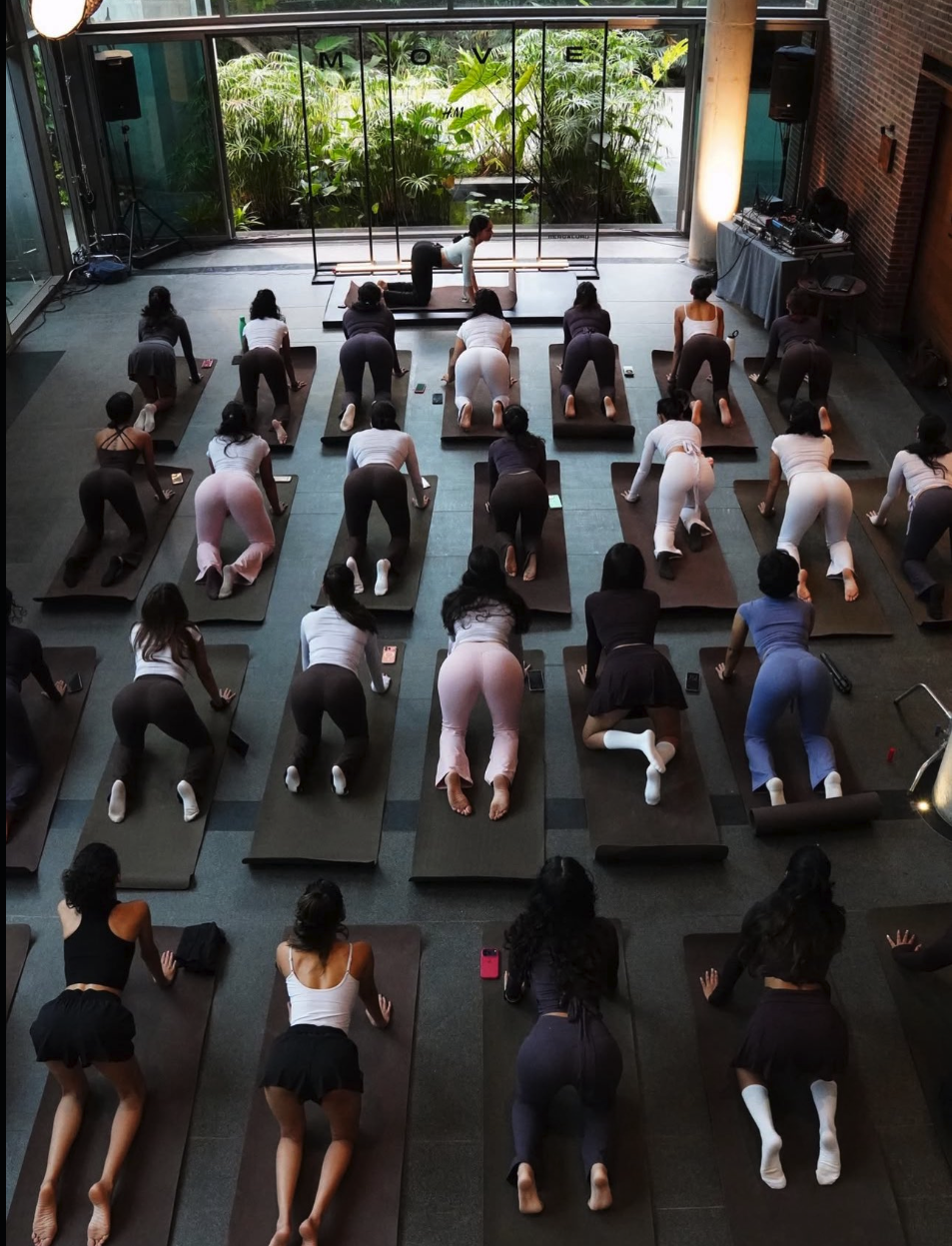 A group of women in athletic wear on yoga mats in a studio, with a male instructor at the front.