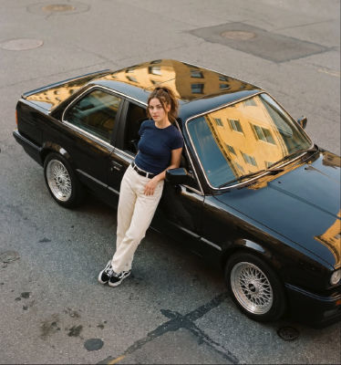 AI-generated image of an unidentified woman leaning against a black BMW