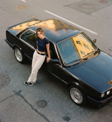 AI-generated image of a woman leaning against a black BMW