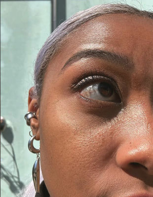 Deepfake close-up selfie of a person with purple hair and hoop earrings